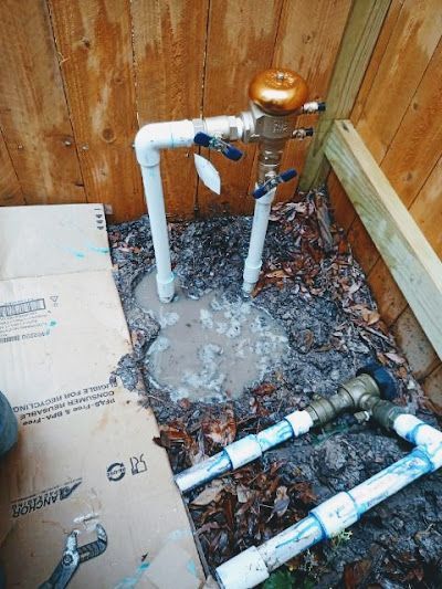 A water meter is sitting on the ground next to a wooden fence.