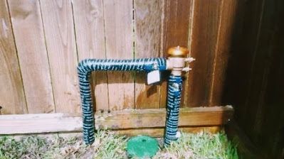 A water pipe is sitting in the grass next to a wooden fence.