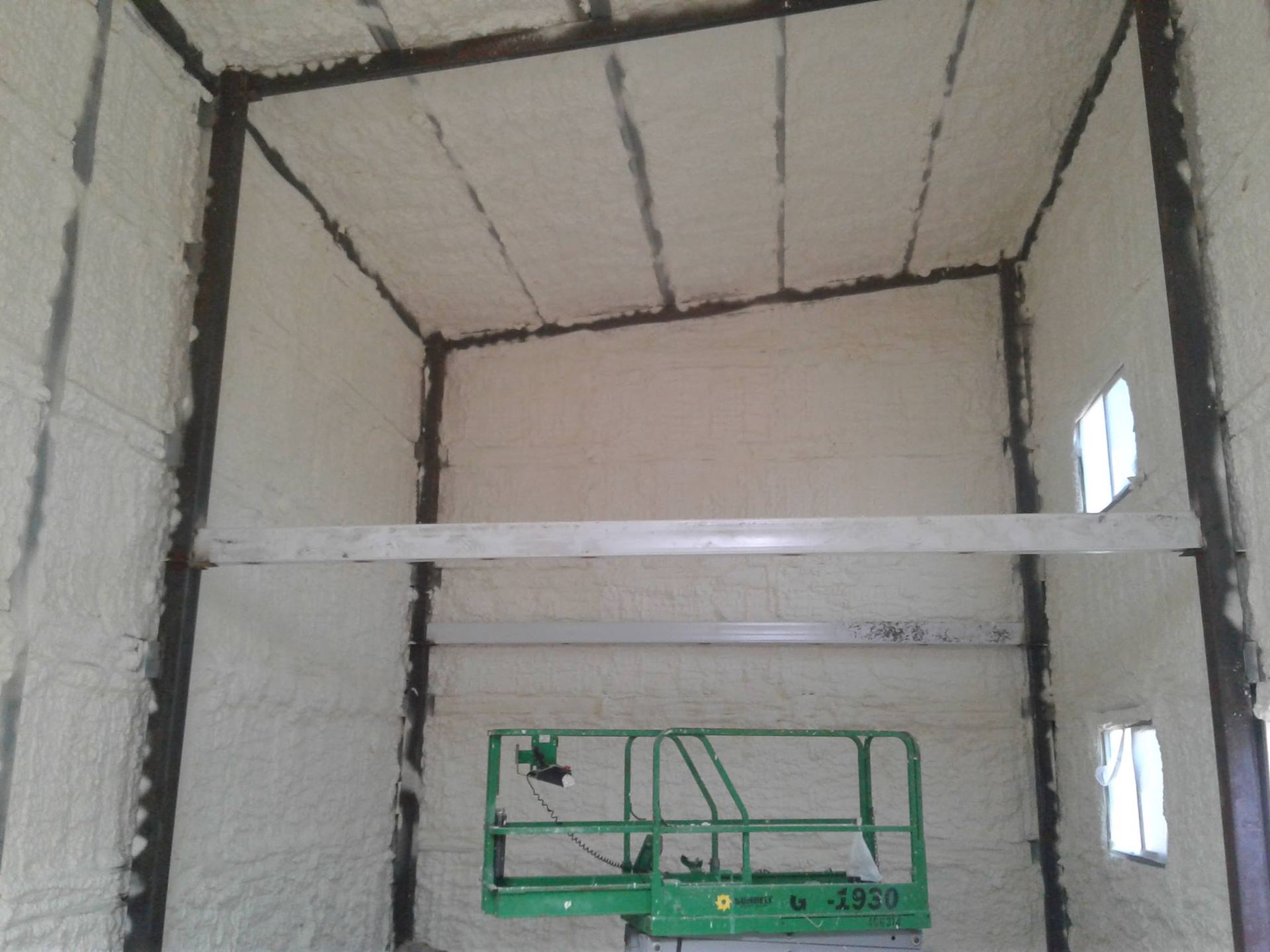A green scissor lift is sitting inside of a building covered in foam.