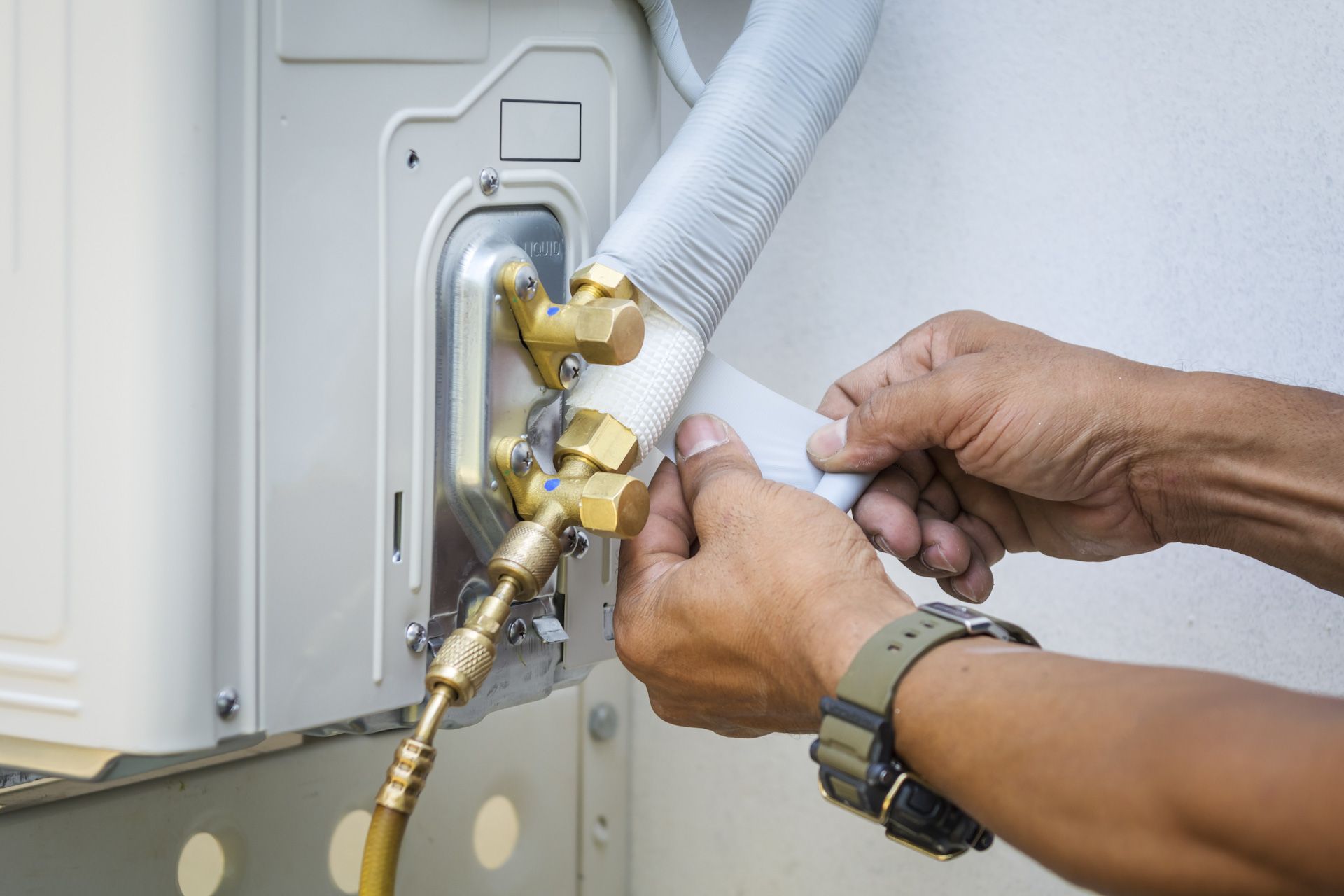 A man is fixing an air conditioner with a wrench.