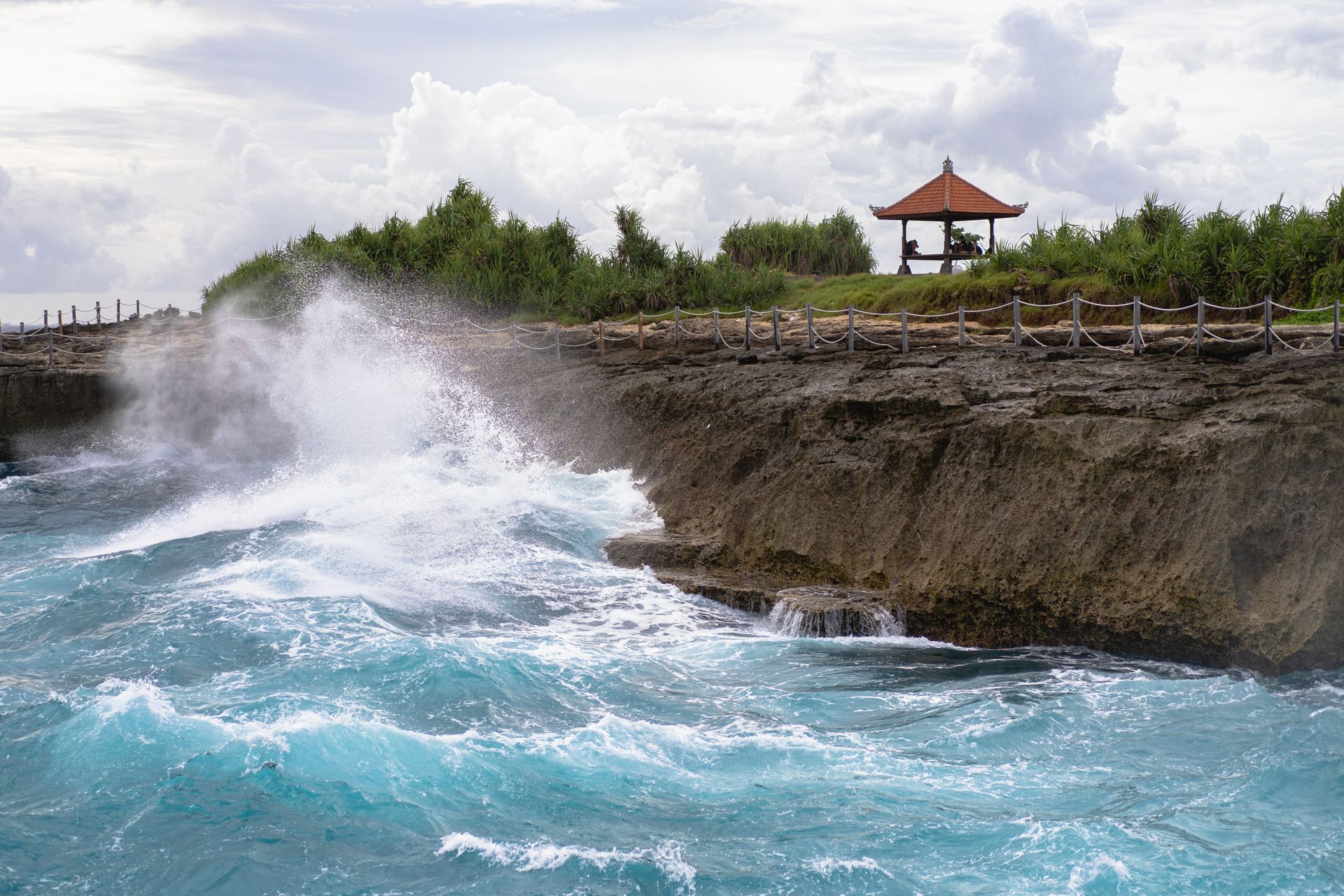 Waves crashing against a rocky cliff with a gazebo in the background.