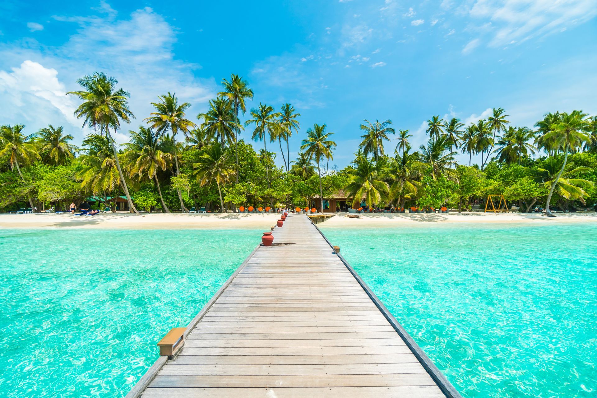 A wooden pier leading to a tropical beach with palm trees.