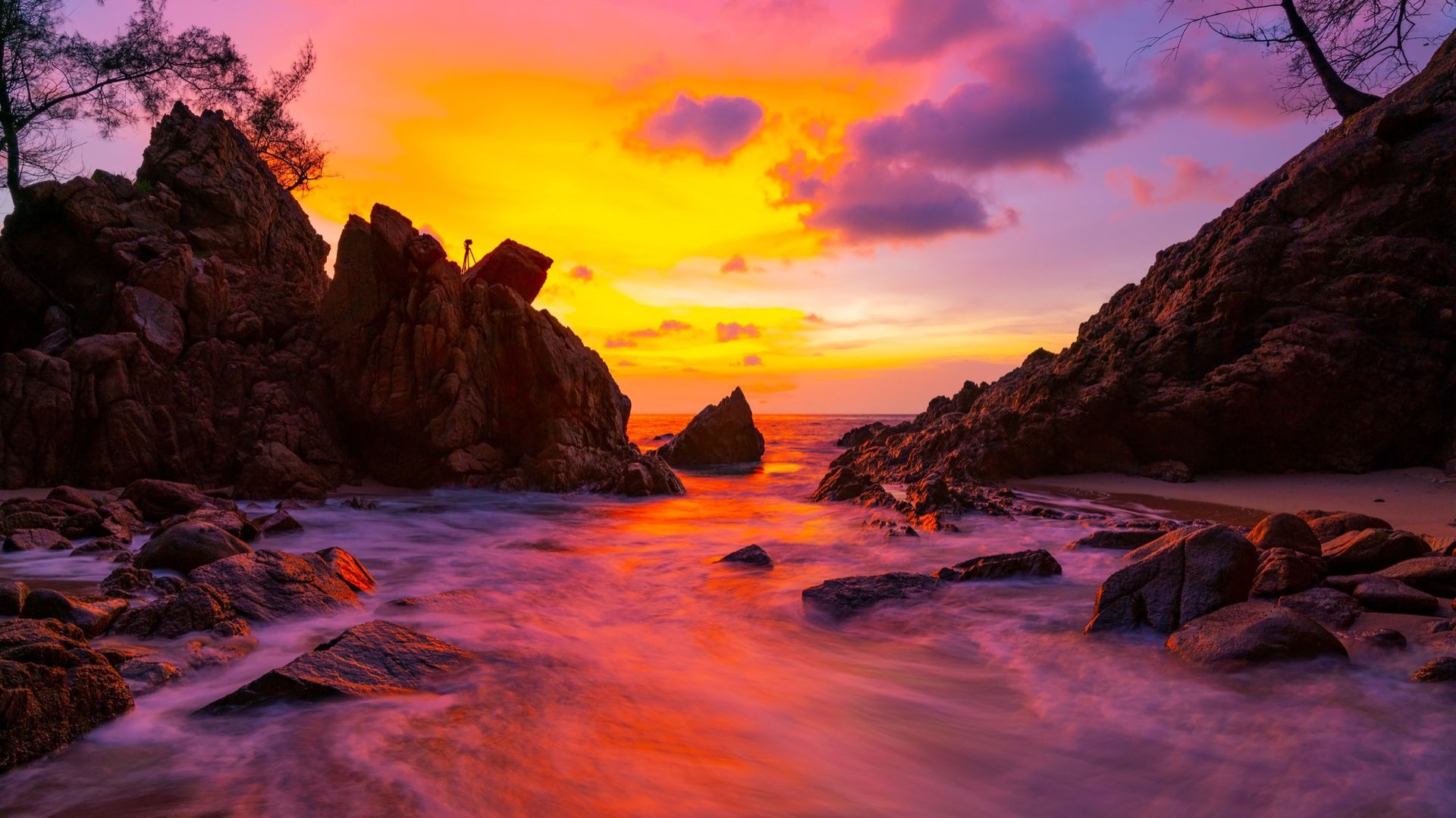 A sunset over a rocky beach with waves crashing against the rocks.