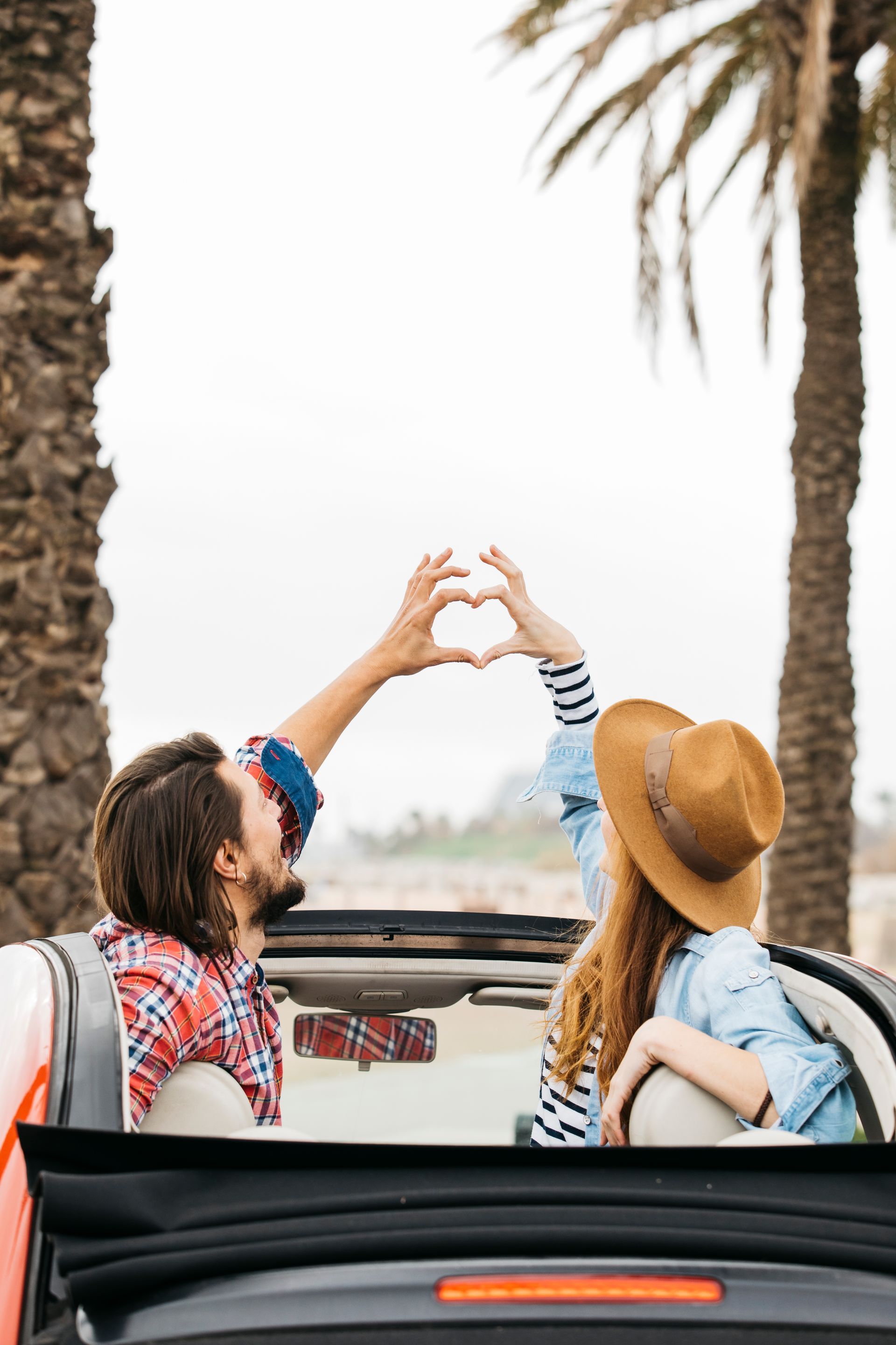 A man and a woman are making a heart shape with their hands in a car.