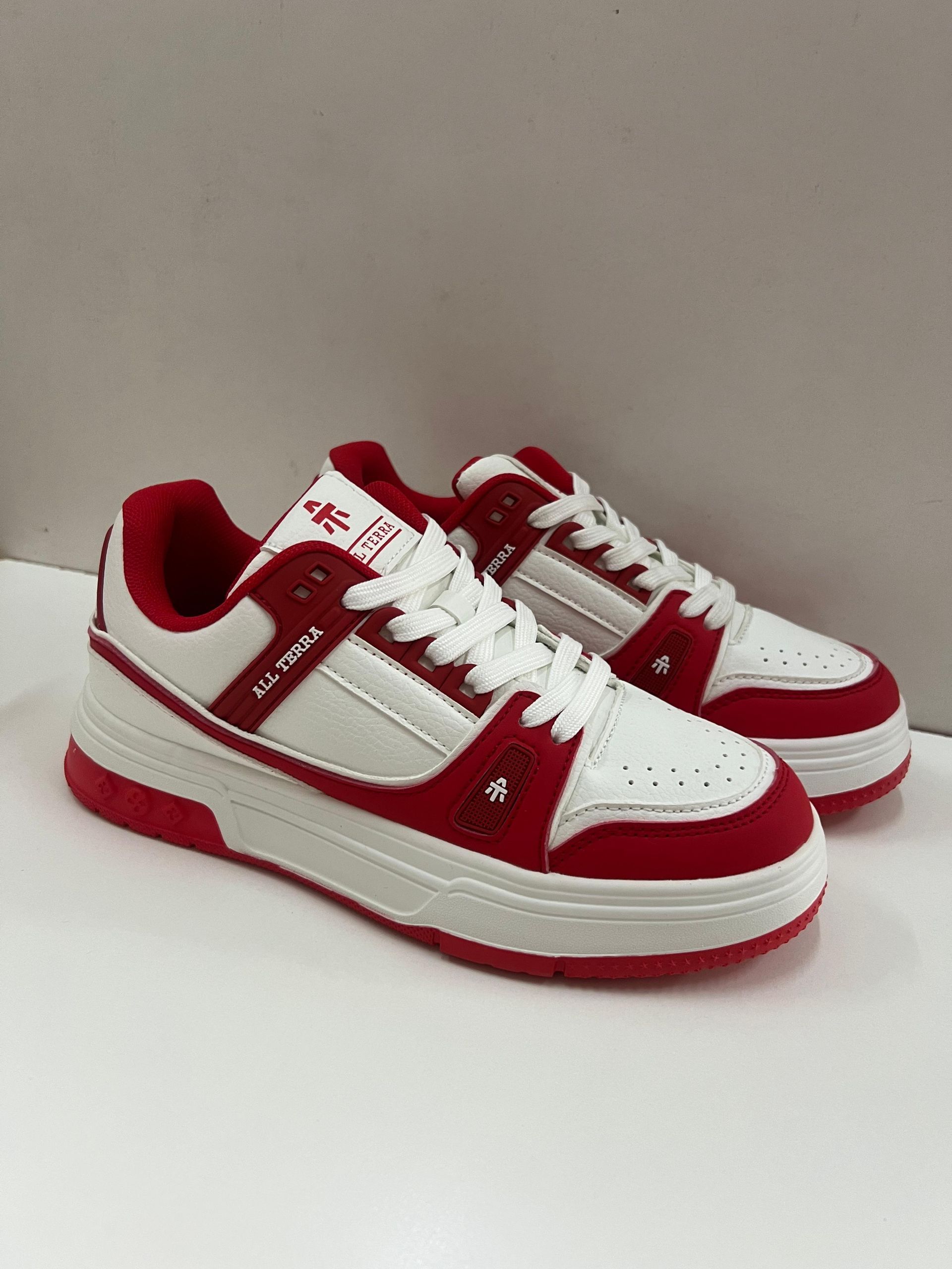 Zapatillas rojas y blancas, vista lateral, sobre una superficie blanca.