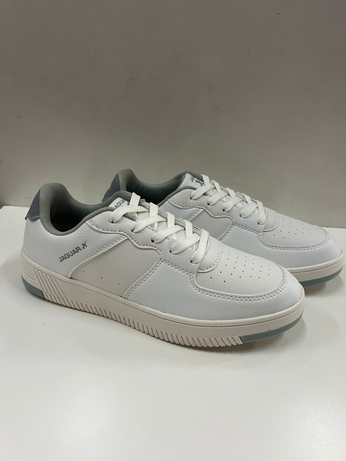 Zapatillas blancas y grises con cordones blancos, colocadas sobre una superficie blanca.