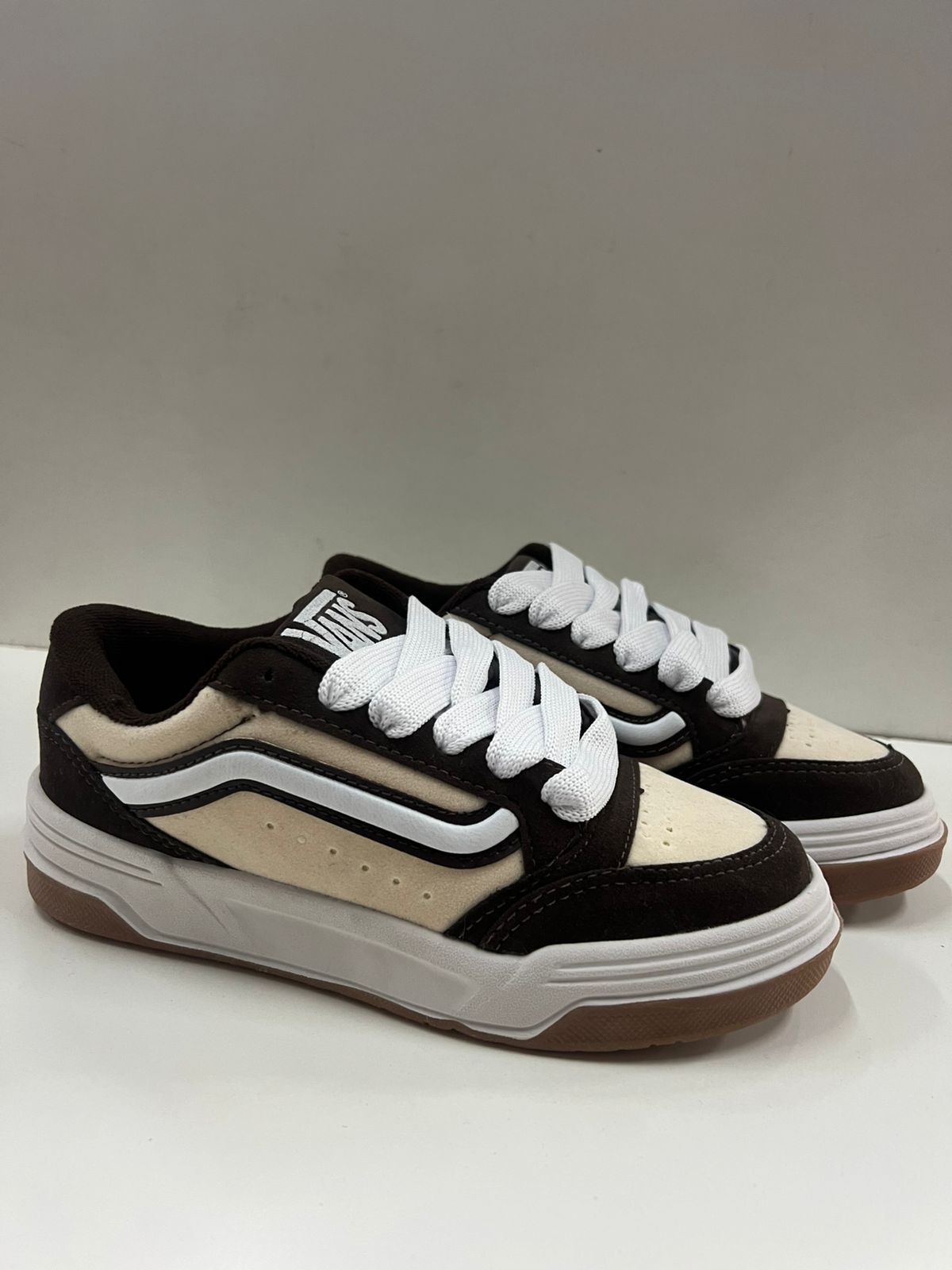 Zapatillas Vans marrones y crema con cordones blancos sobre una superficie blanca.