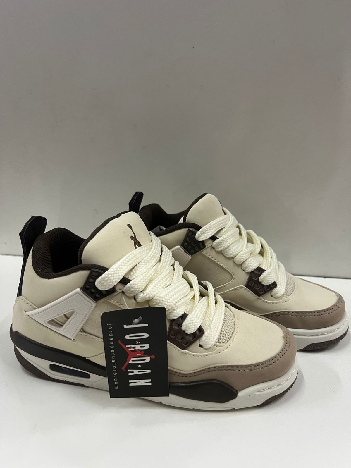 Par de zapatillas Air Jordan 4 para bebé en color crema, marrón y negro, con etiqueta colgante.