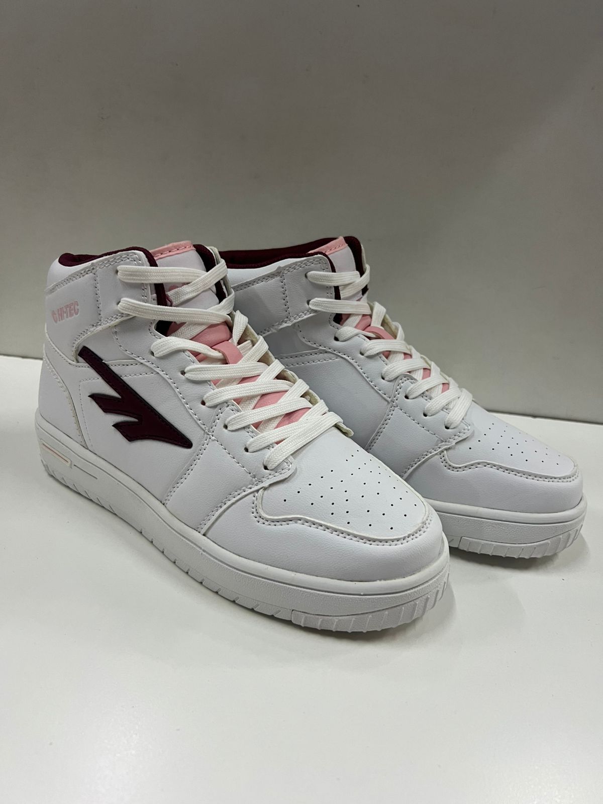 Zapatillas blancas de caña alta con detalles en burdeos y rosa, sobre una superficie blanca.