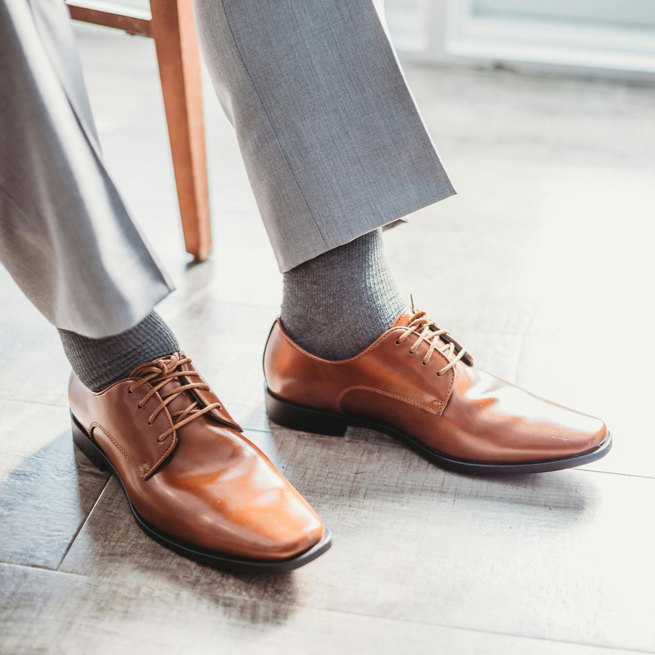 Piernas y pies de un hombre con pantalones grises, calcetines grises y zapatos de vestir de cuero marrón.