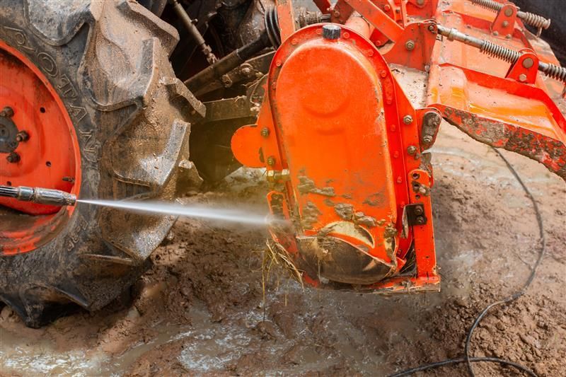 An orange tractor component is being cleaned with a high-pressure water stream.