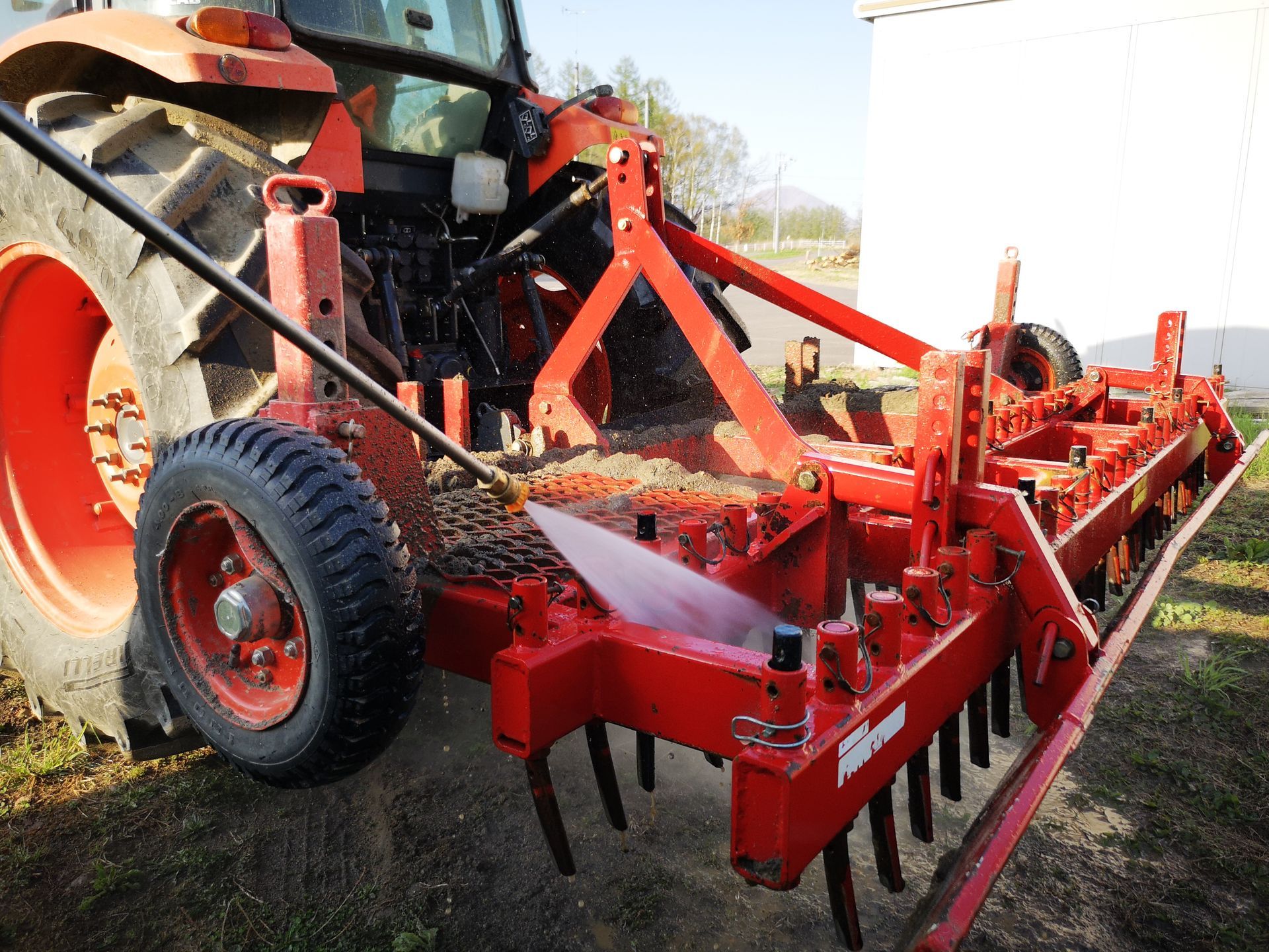 Red tractor with a tiller attached, in a grassy field.