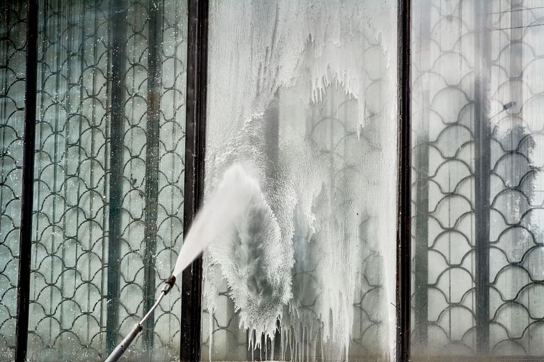 A person using a power washer to clean a glass window with decorative paneling.