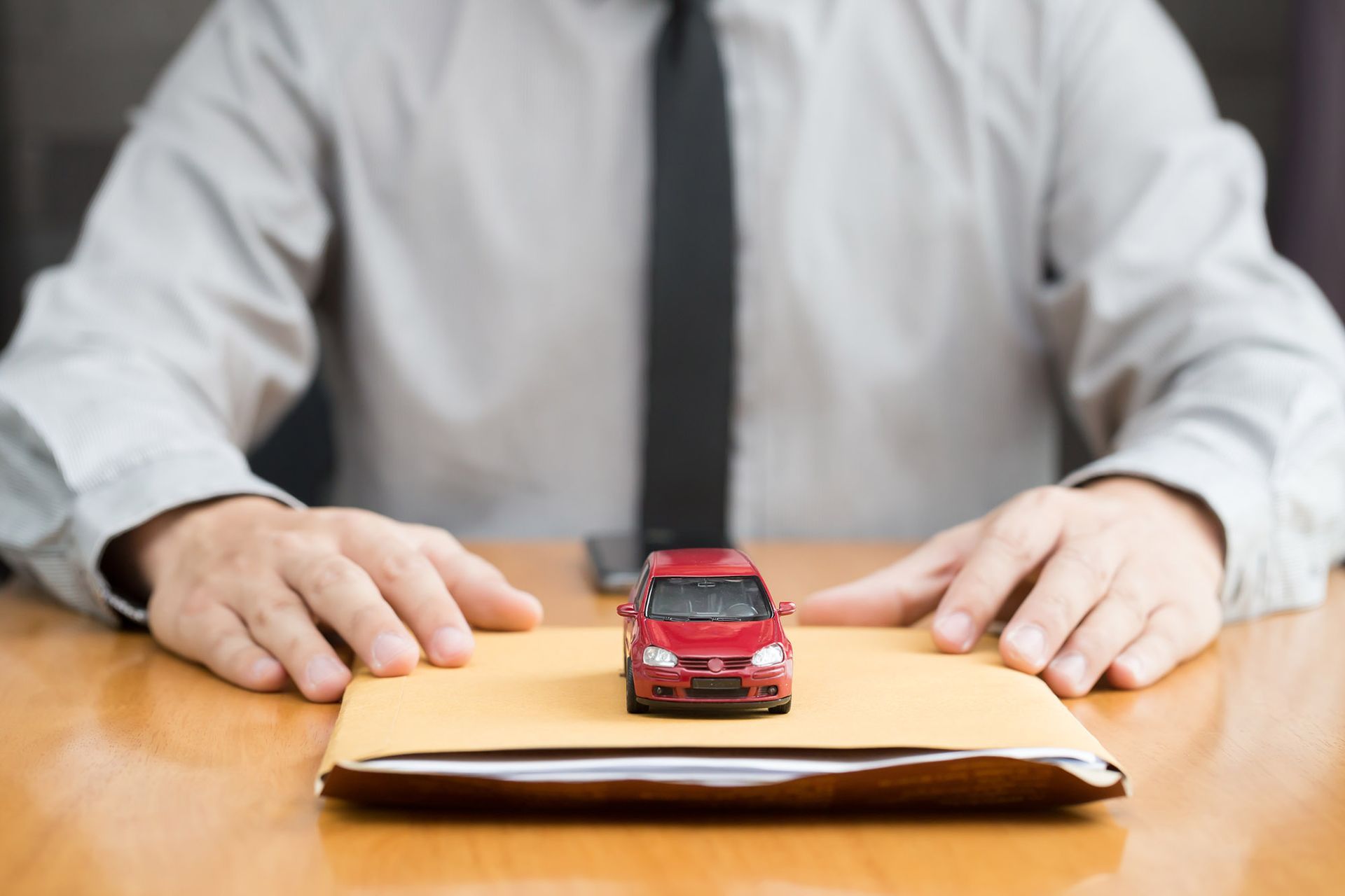 Man in tie with hands resting on envelope; red toy car on top.