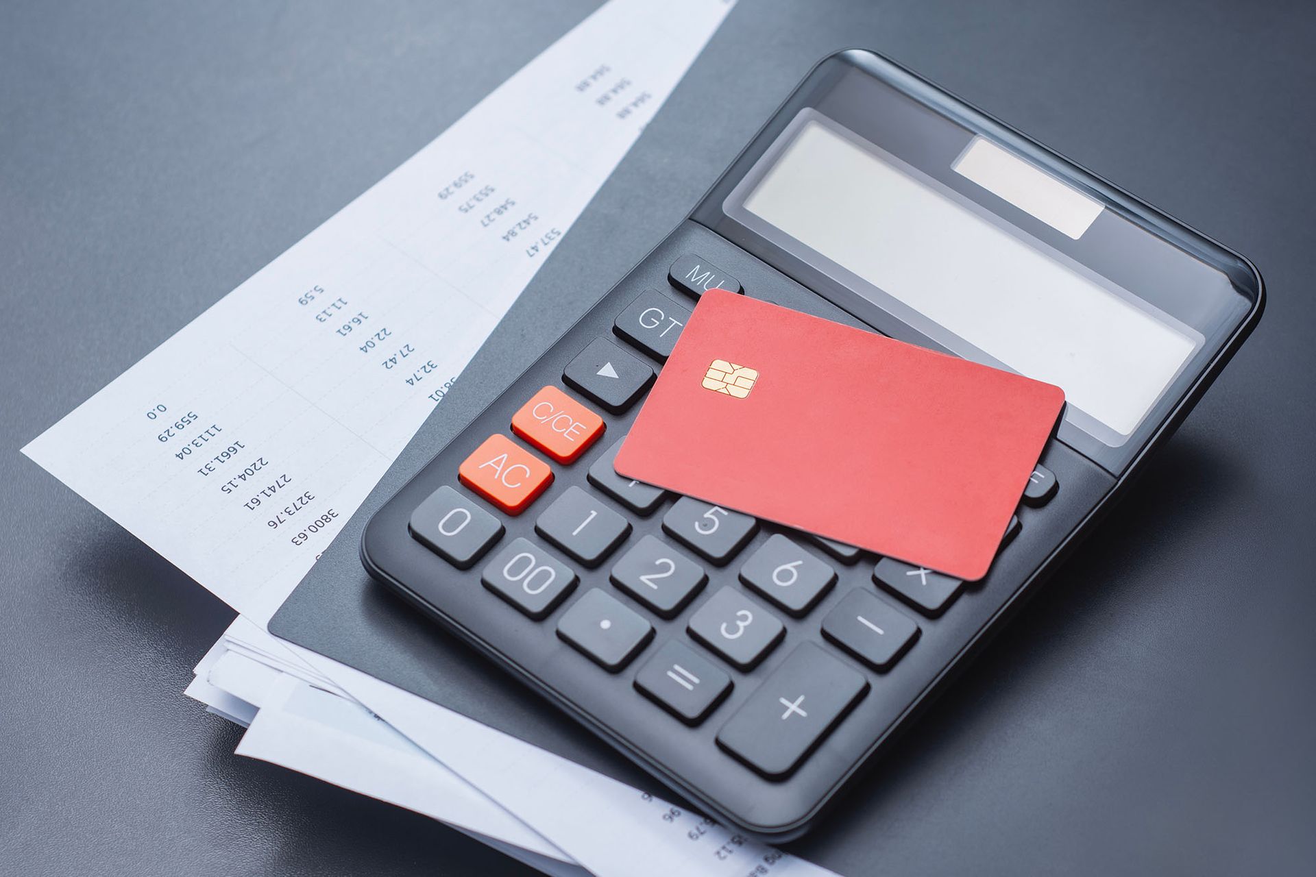 Calculator, red credit card, and receipts on a dark surface.