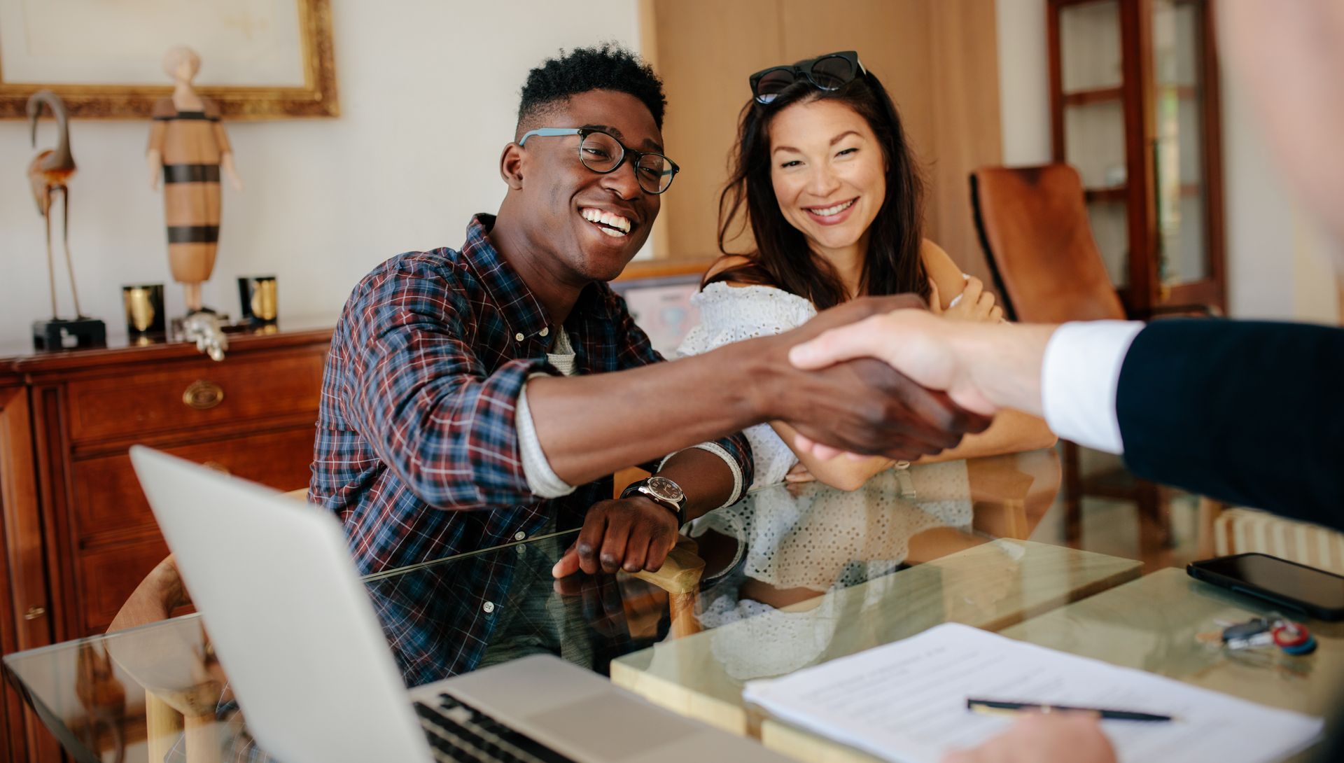 Two first-home buyers are smiling and handshaking the realtor after signing the contract. Two first-home buyers are smiling and handshaking the realtor after signing the contract.