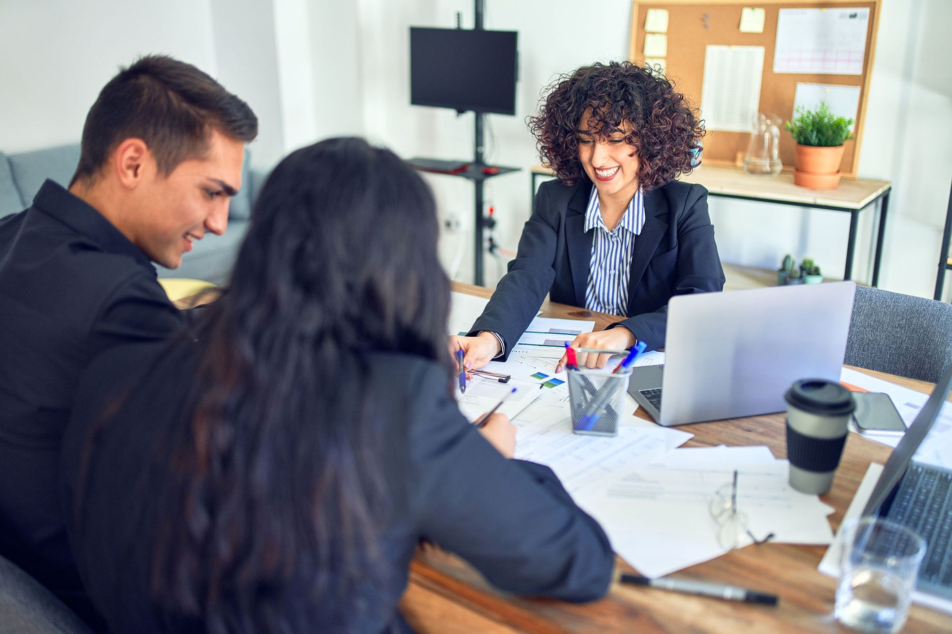 Three people reviewing paperwork at a table; one points, smiling.