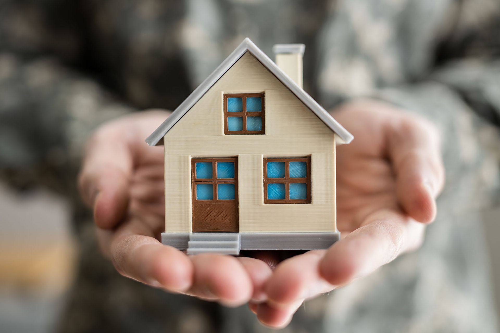Hands holding a miniature house, possibly a military person offering housing.