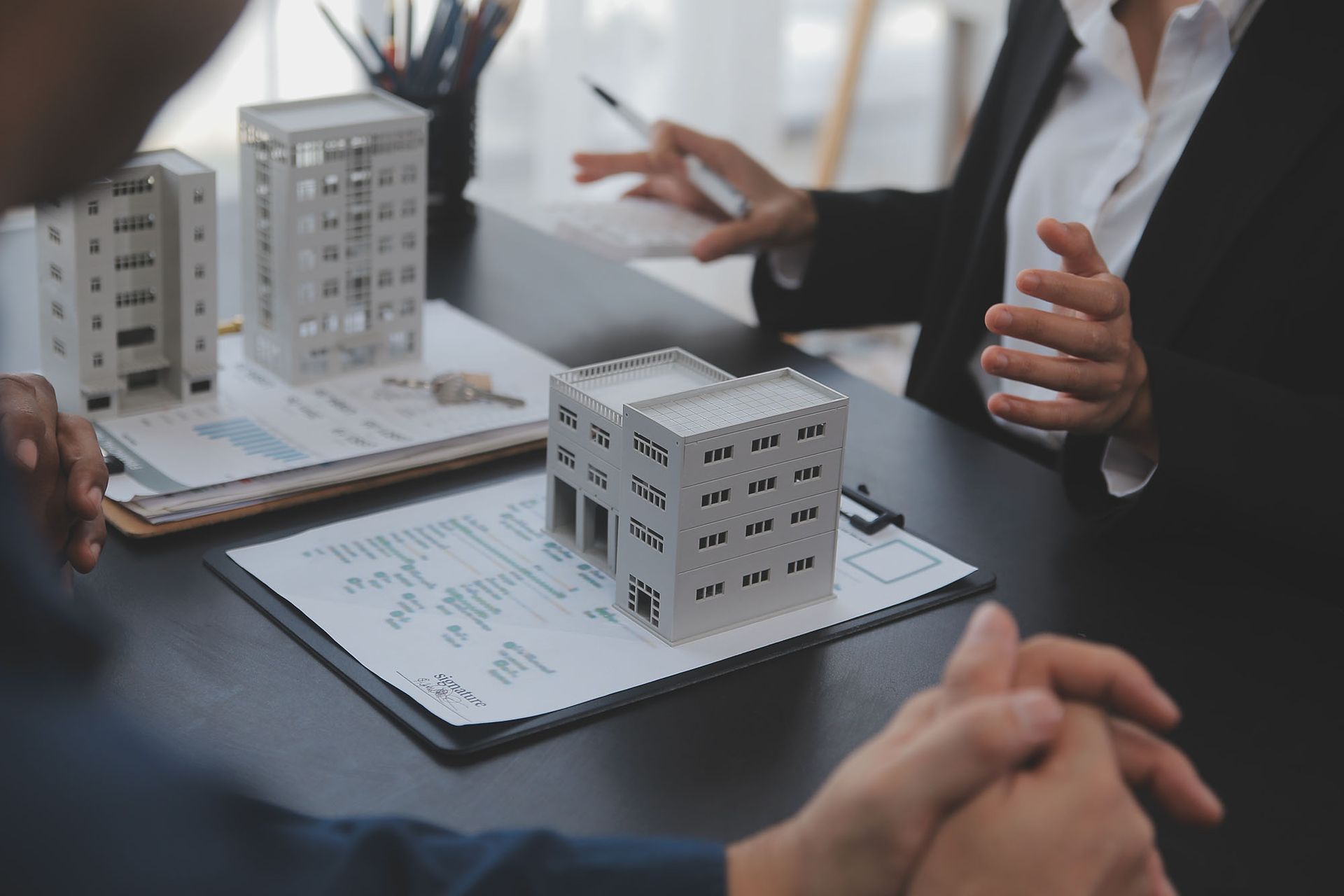 Real estate agents discussing documents with a client, miniature building models on table.