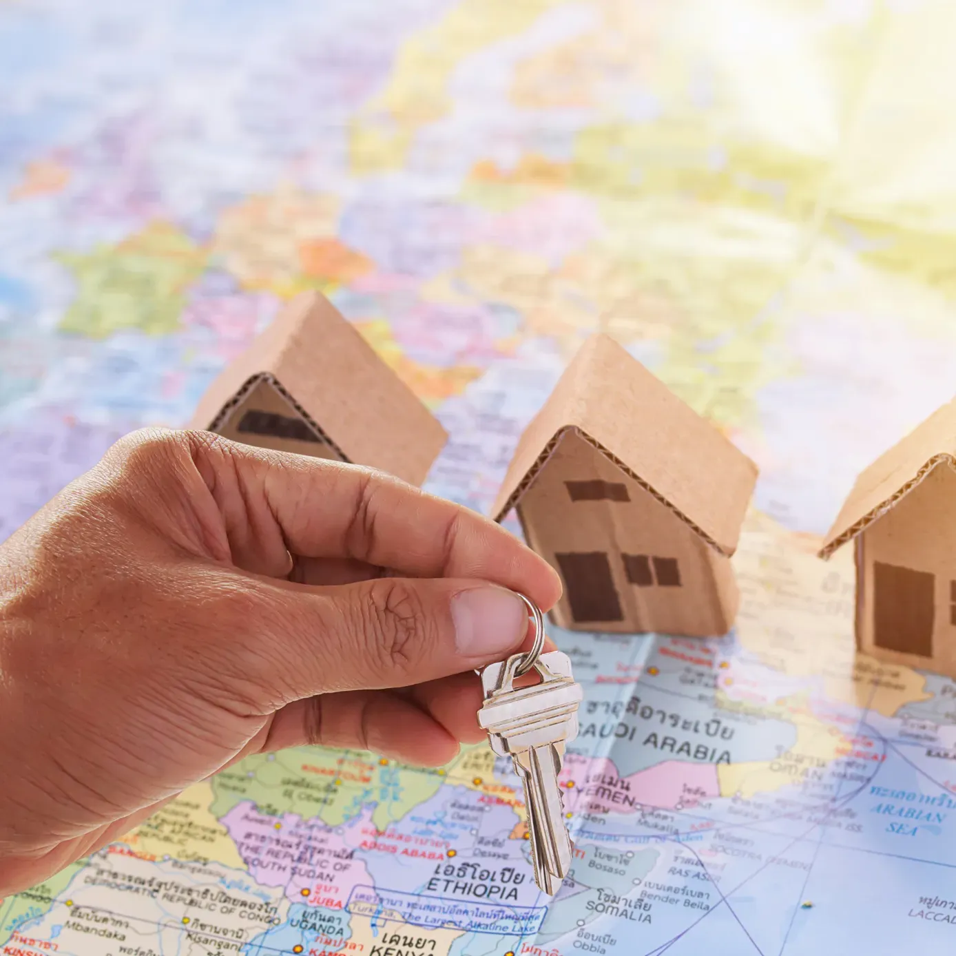 Hand holding a key over a world map, with cardboard houses in the background.