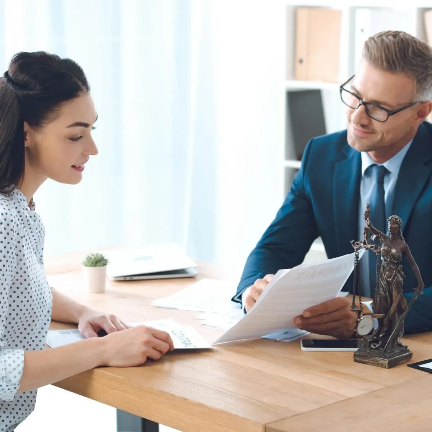 Woman and man reviewing documents at a desk; a statue of Lady Justice is visible.