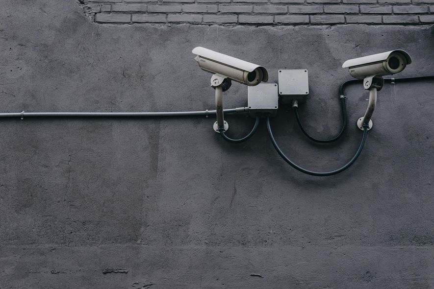 Two security cameras mounted on a concrete wall, wired to a central box.