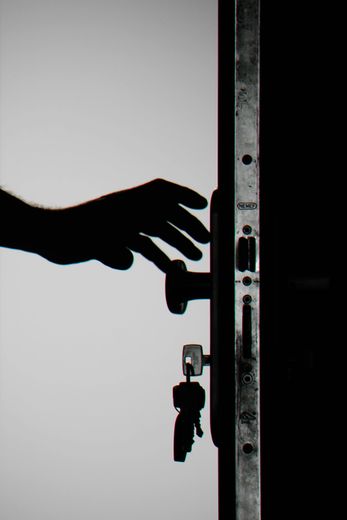Silhouette of hand reaching for door handle with keys in the lock.