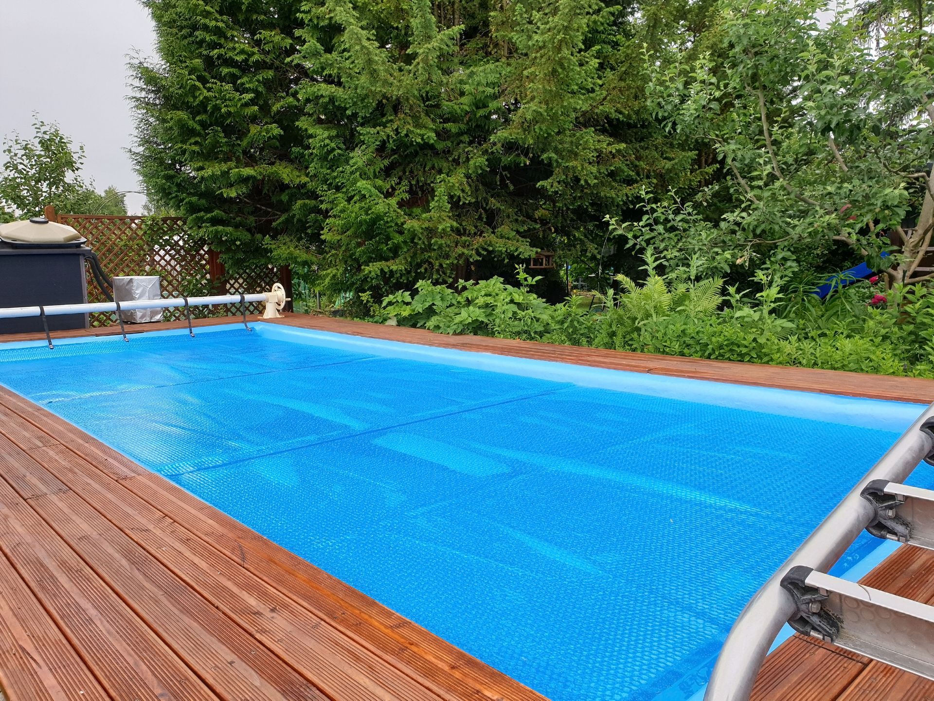 A large blue swimming pool is surrounded by trees and a wooden deck.