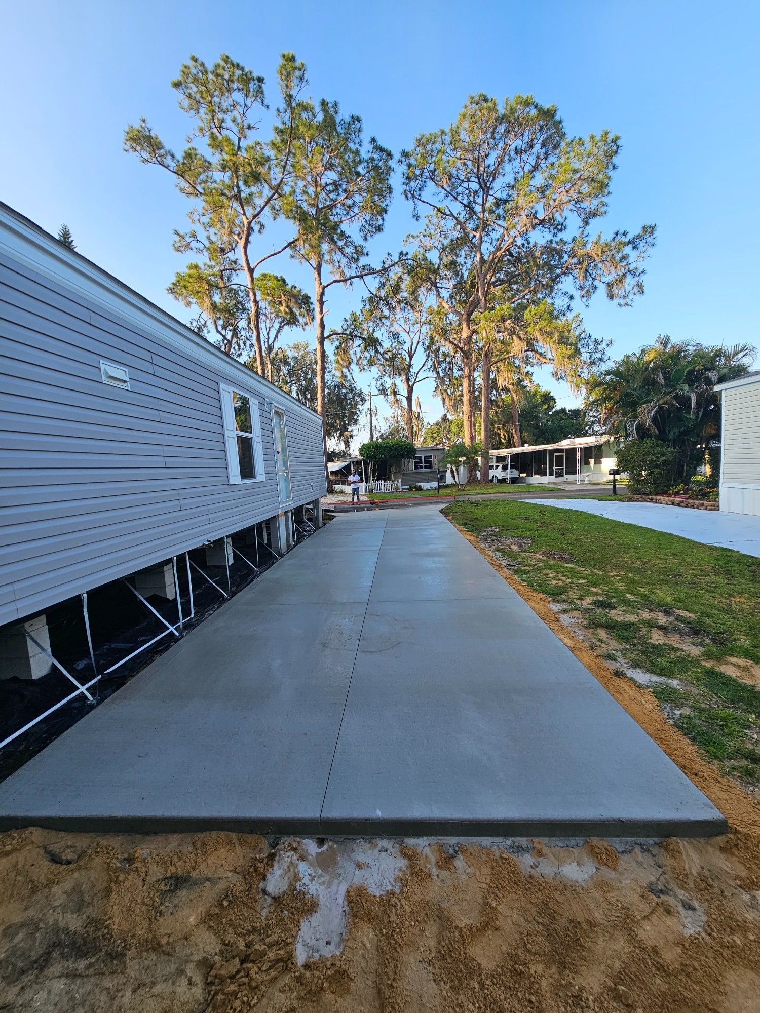 New concrete driveway next to a light blue mobile home, sunny day.
