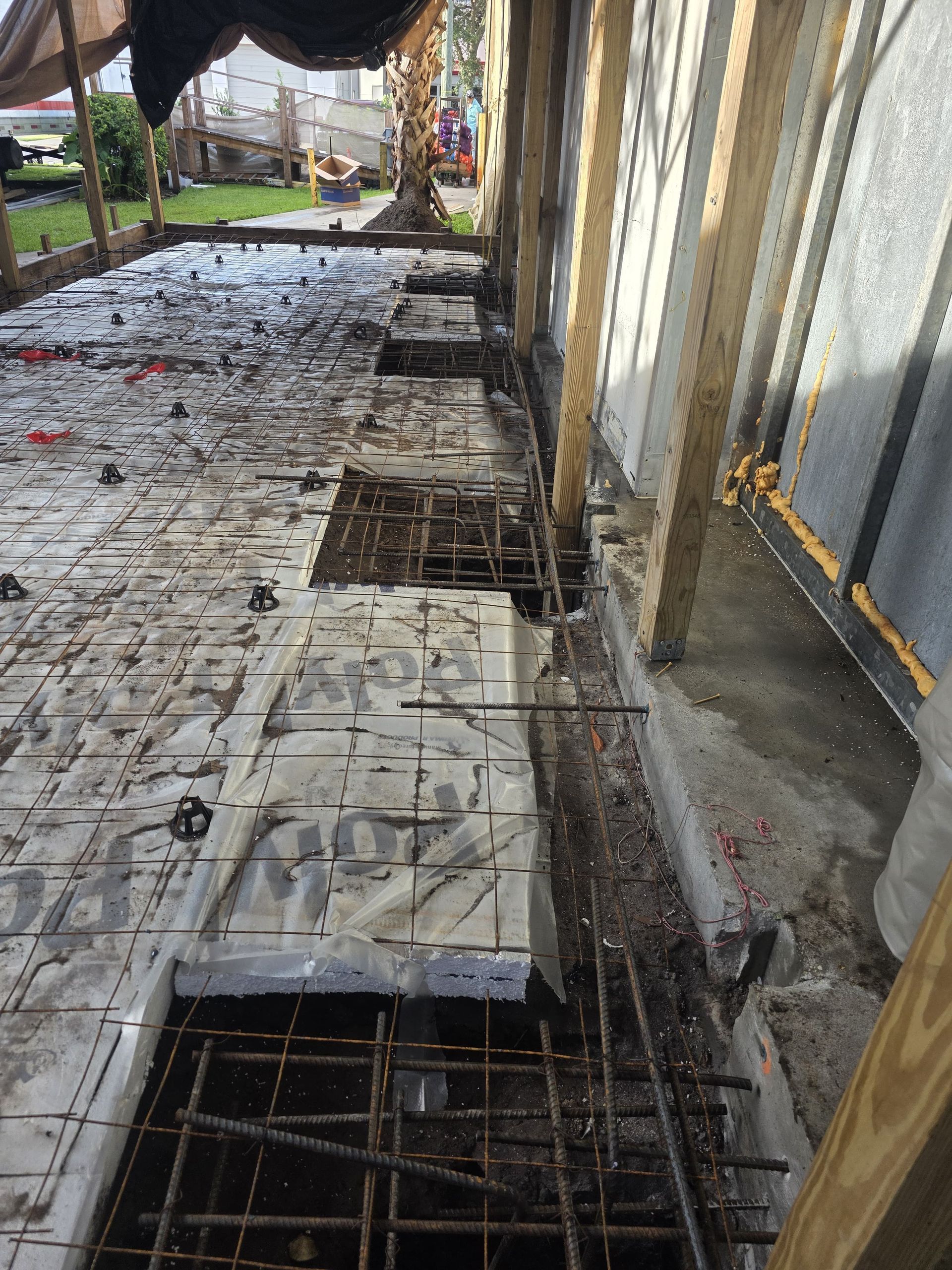 Construction site: concrete foundation with rebar and formwork. Sunlight, gray and brown tones.