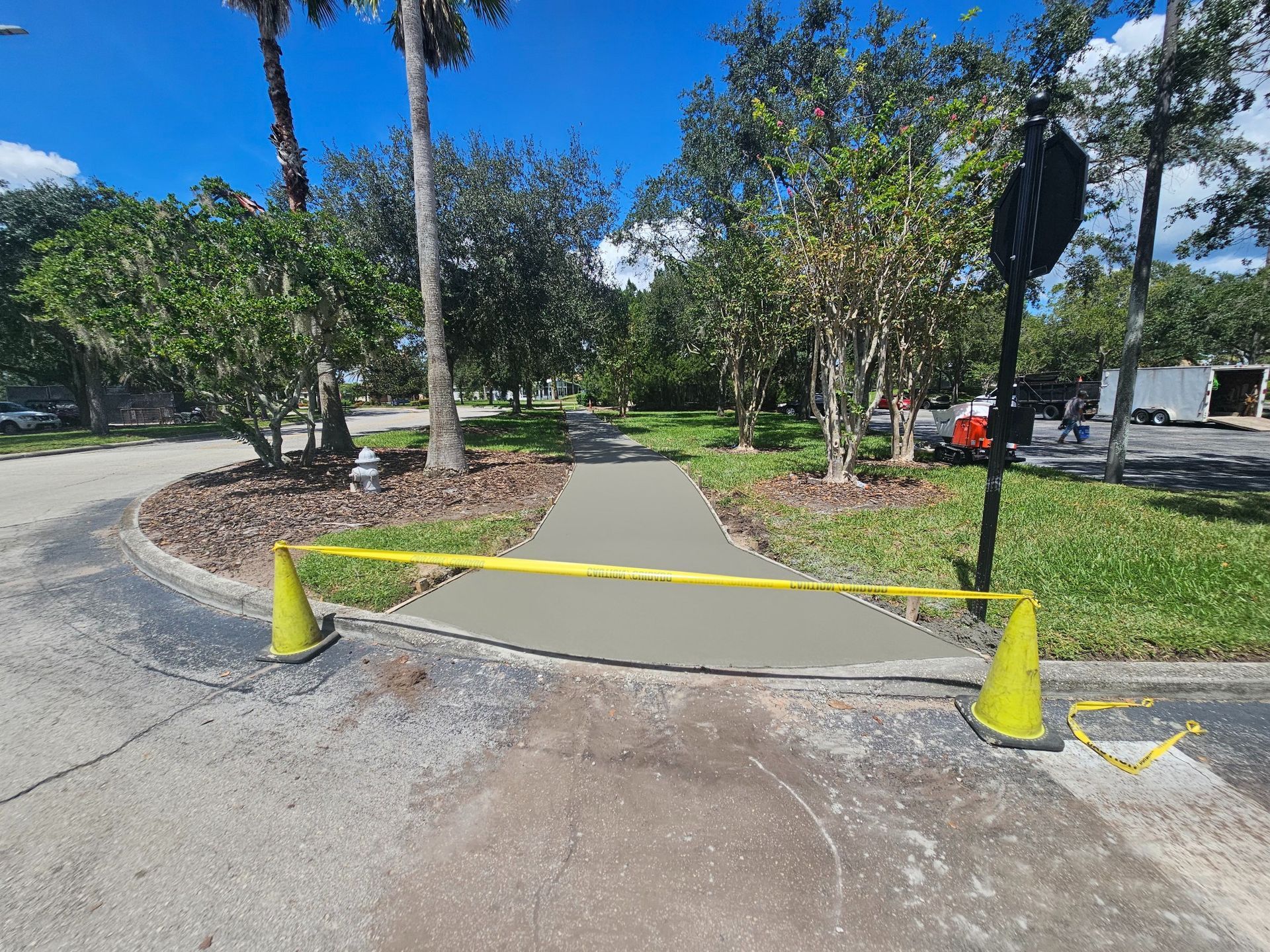 Freshly poured concrete sidewalk blocked by cones and yellow tape.