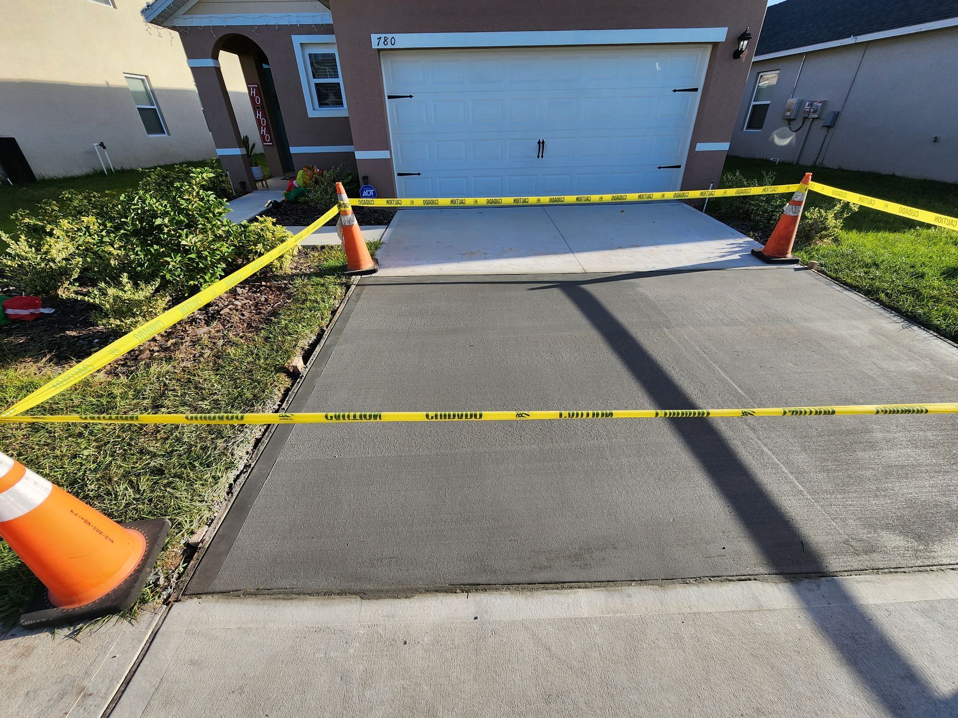 A concrete driveway is surrounded by yellow tape and orange cones.