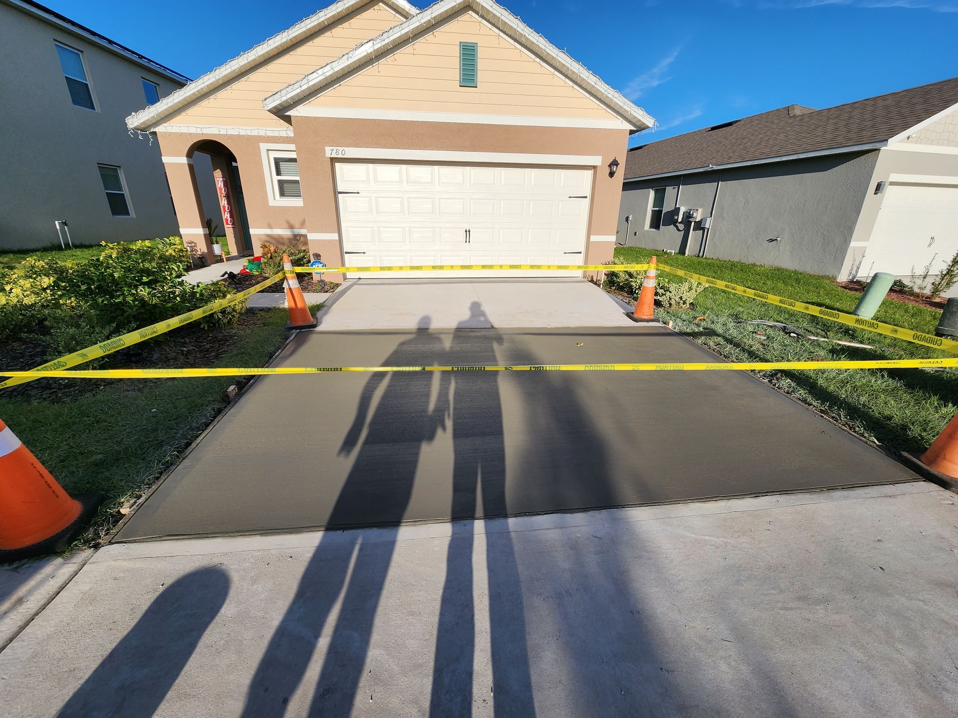 A shadow of a person is cast on a concrete driveway in front of a house.