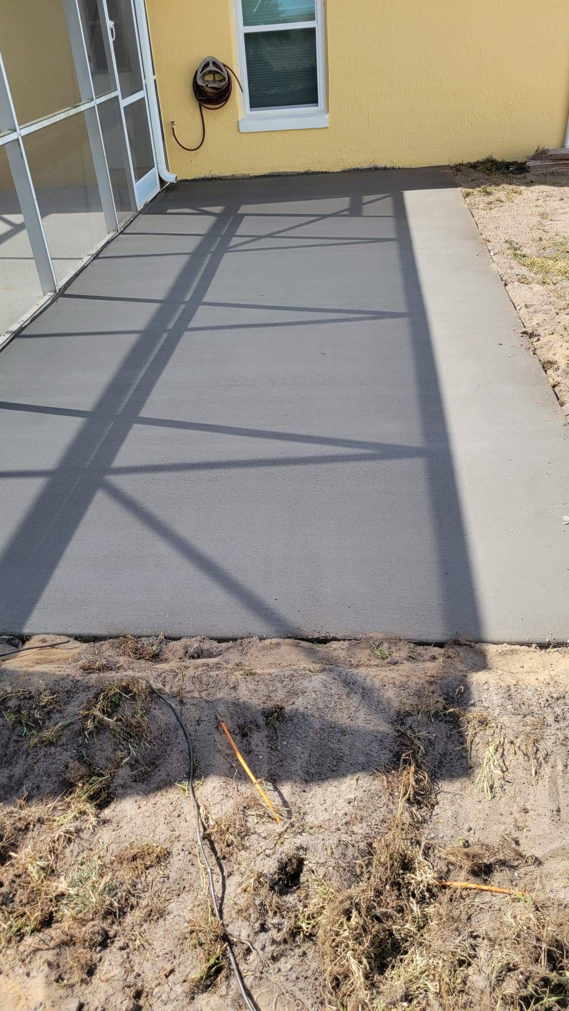 A concrete driveway is being built in front of a yellow house.