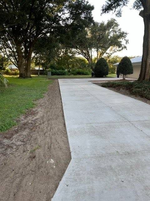 A concrete driveway leading to a house with trees in the background
