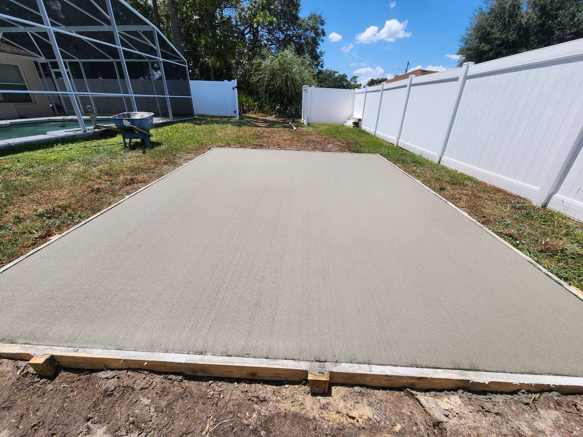 A concrete floor is being built in a backyard next to a pool.
