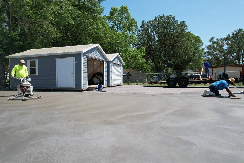 A man is laying concrete in a driveway in front of a garage.