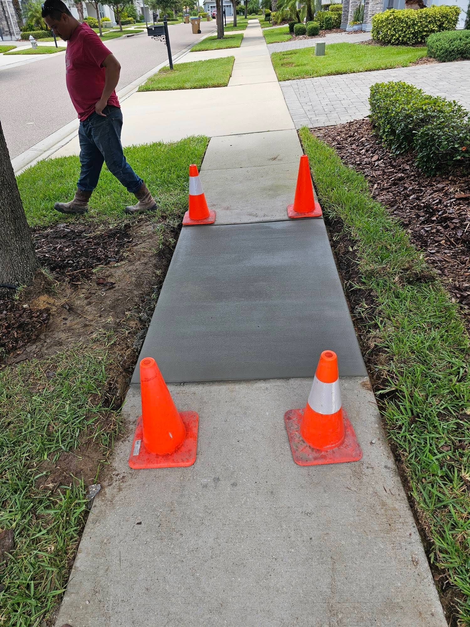 A man is walking down a sidewalk with orange cones on it.