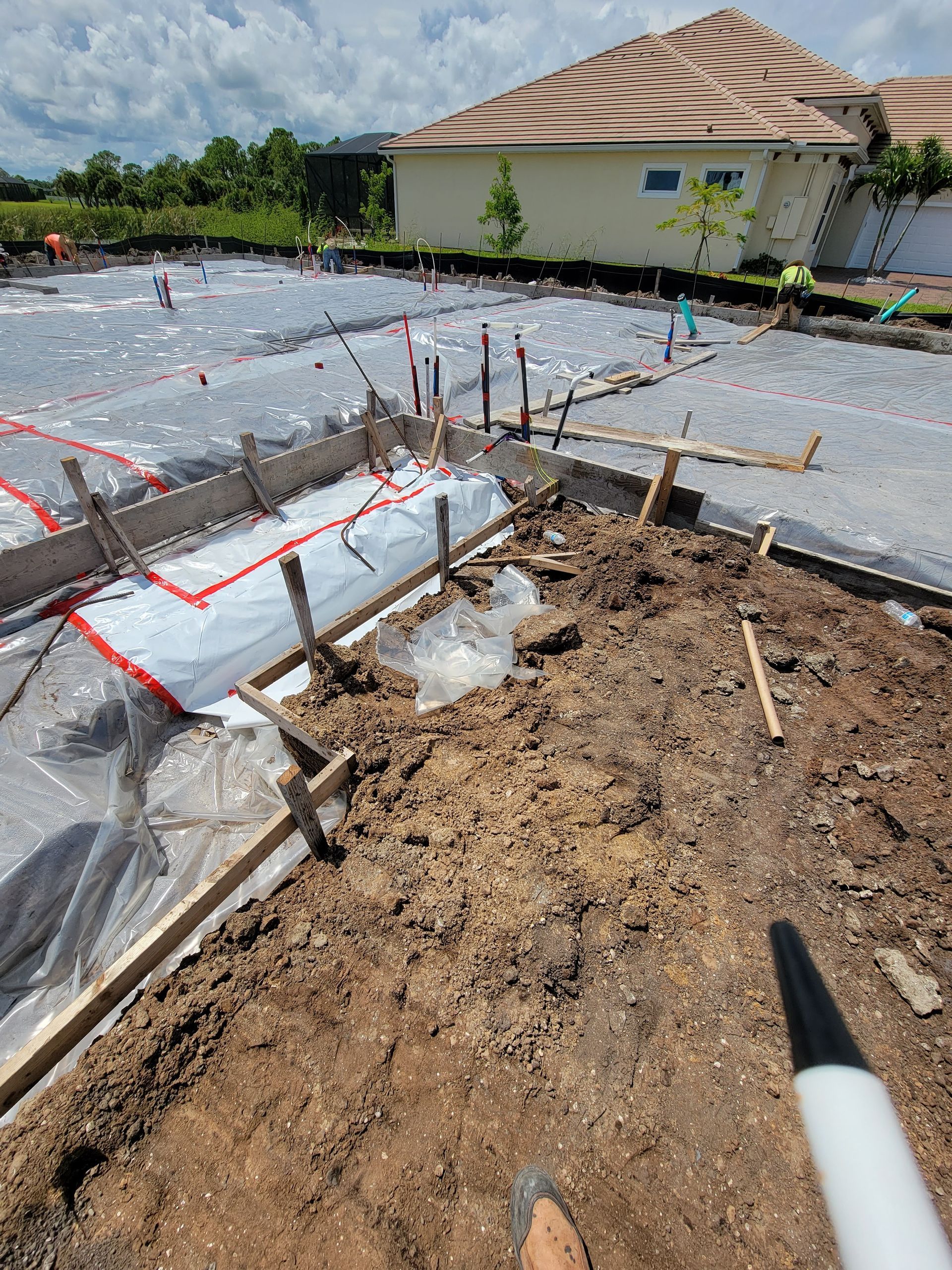 A person is standing in the dirt with a marker in front of a house under construction.