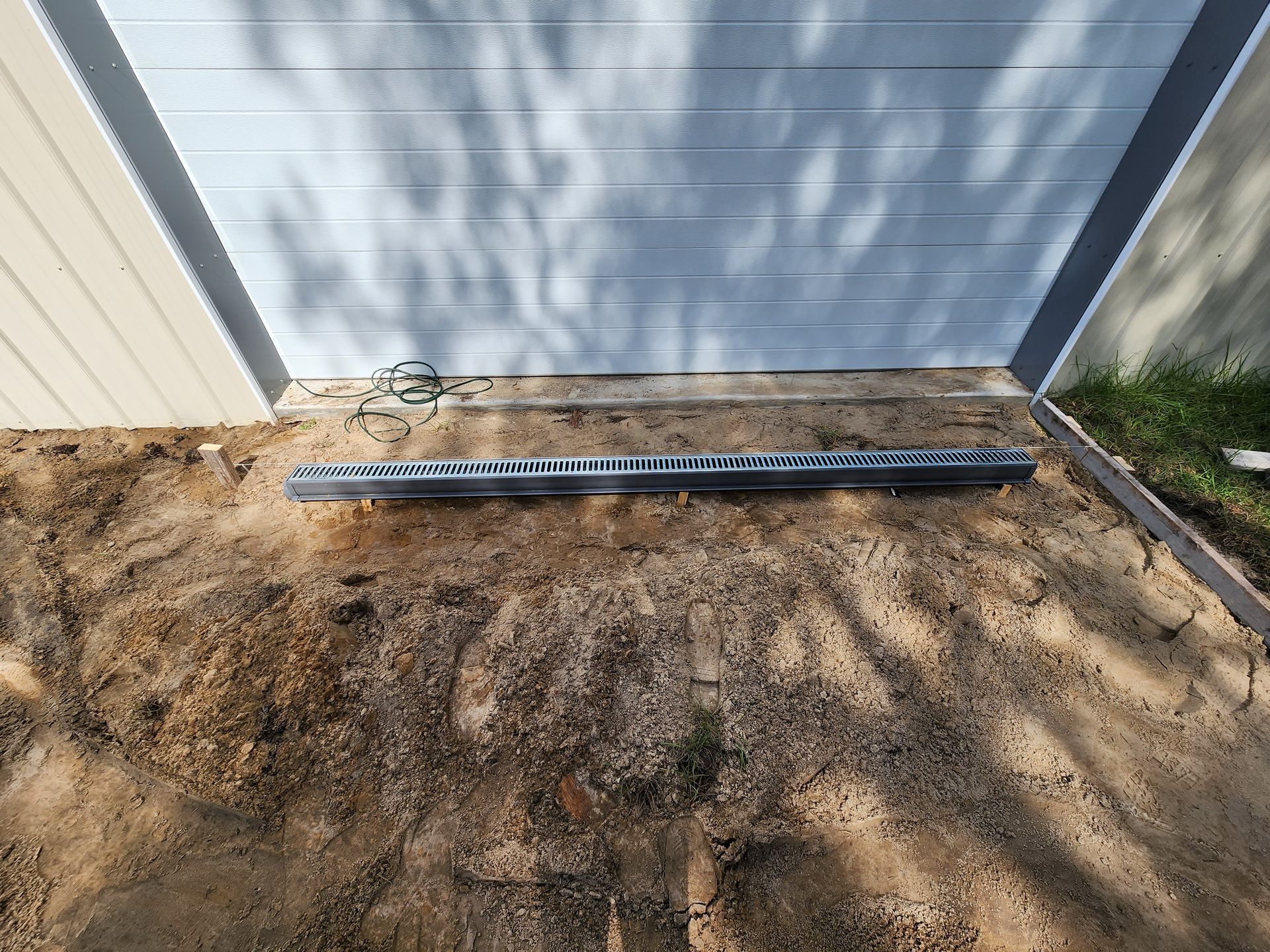 A piece of metal is sitting in the dirt in front of a garage door.