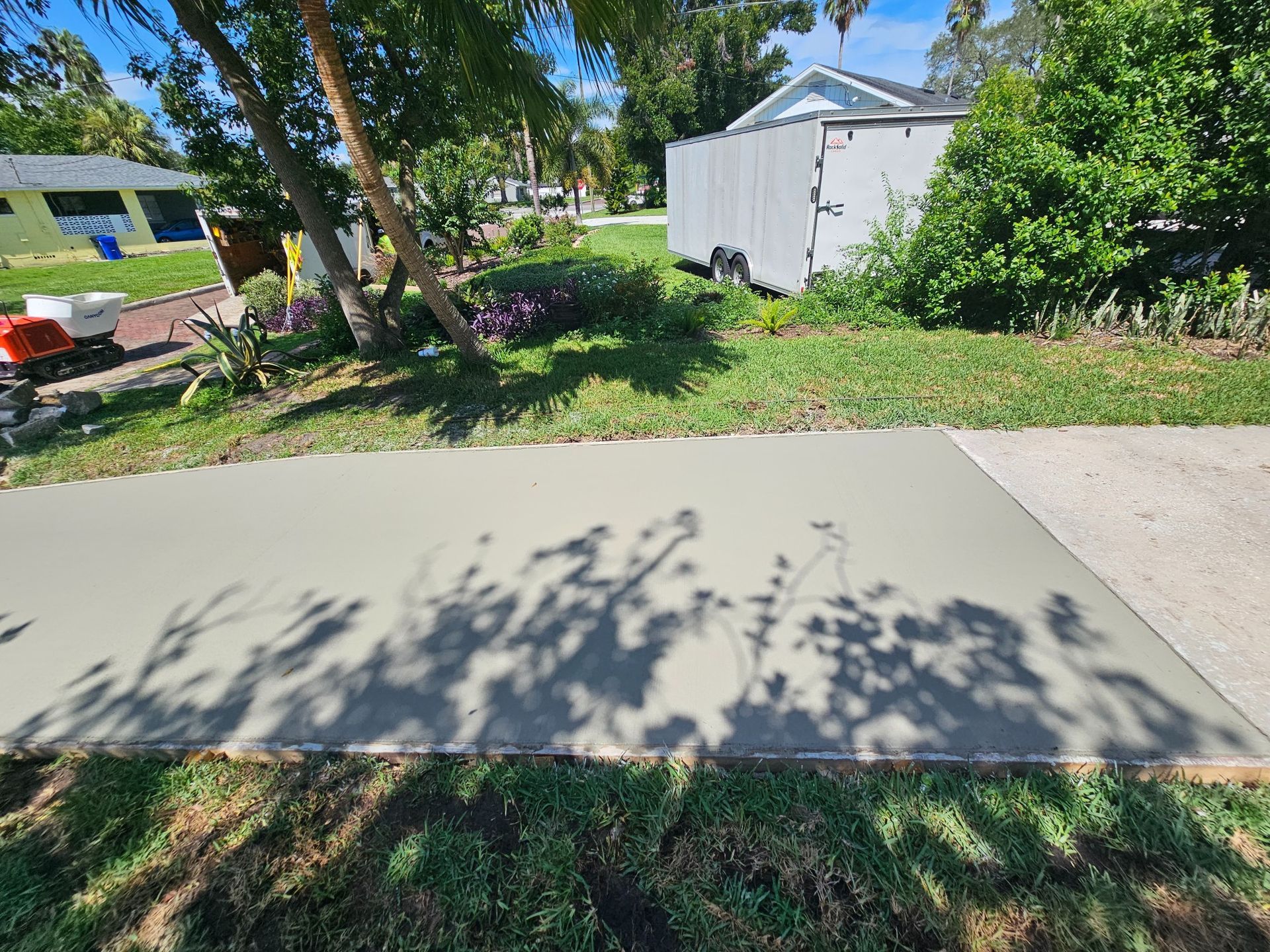 Freshly poured concrete slab in a yard, casting shadows.