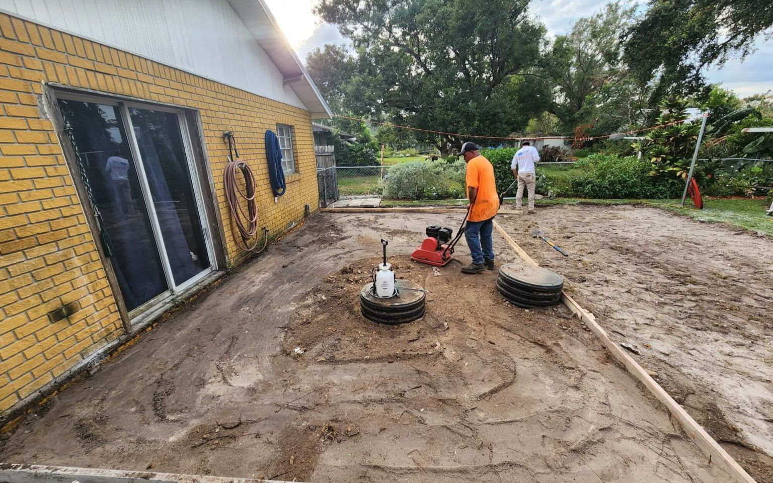 A man is standing in the dirt in front of a house.