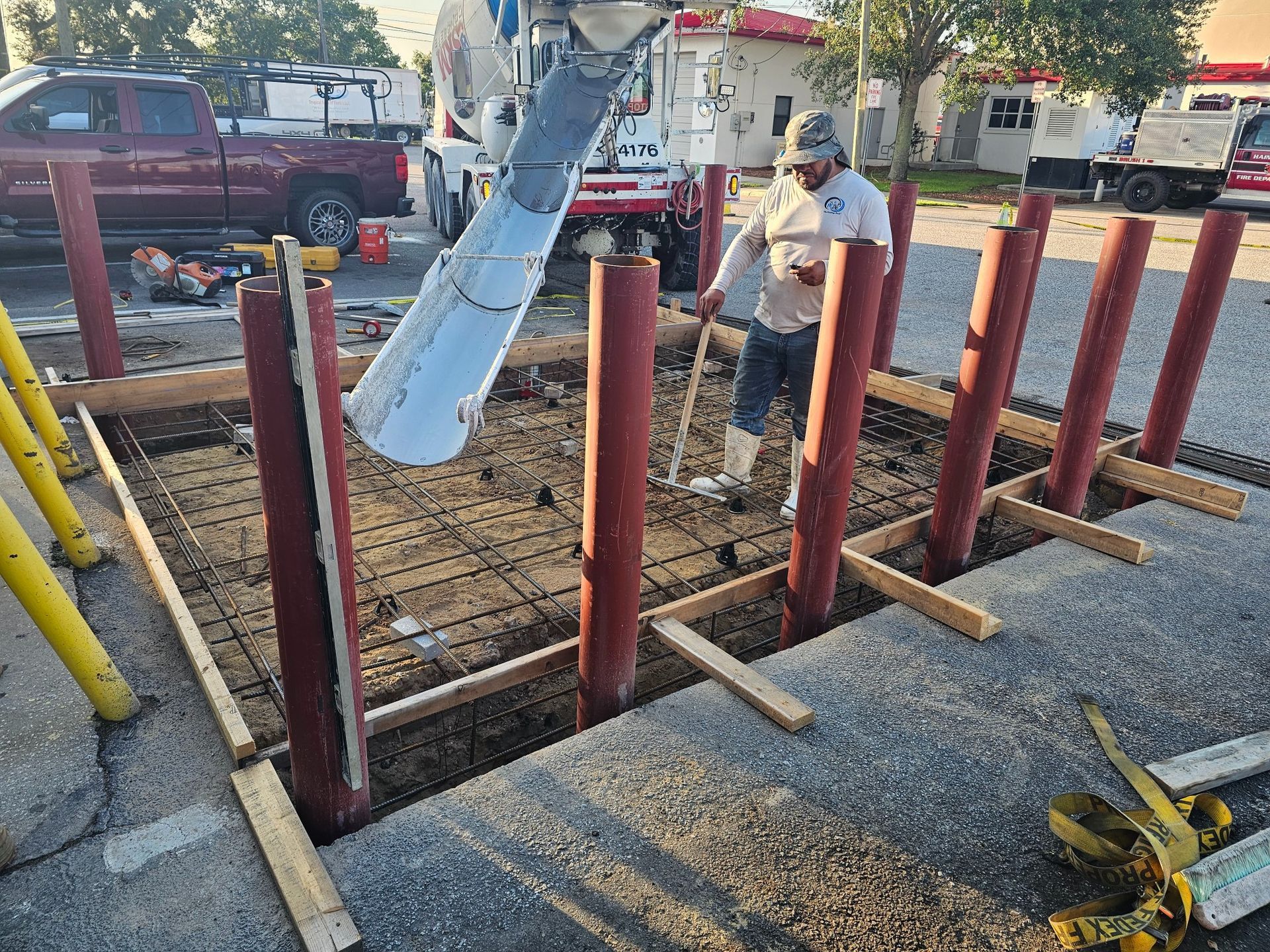 Construction workers pouring concrete into a foundation with red columns.