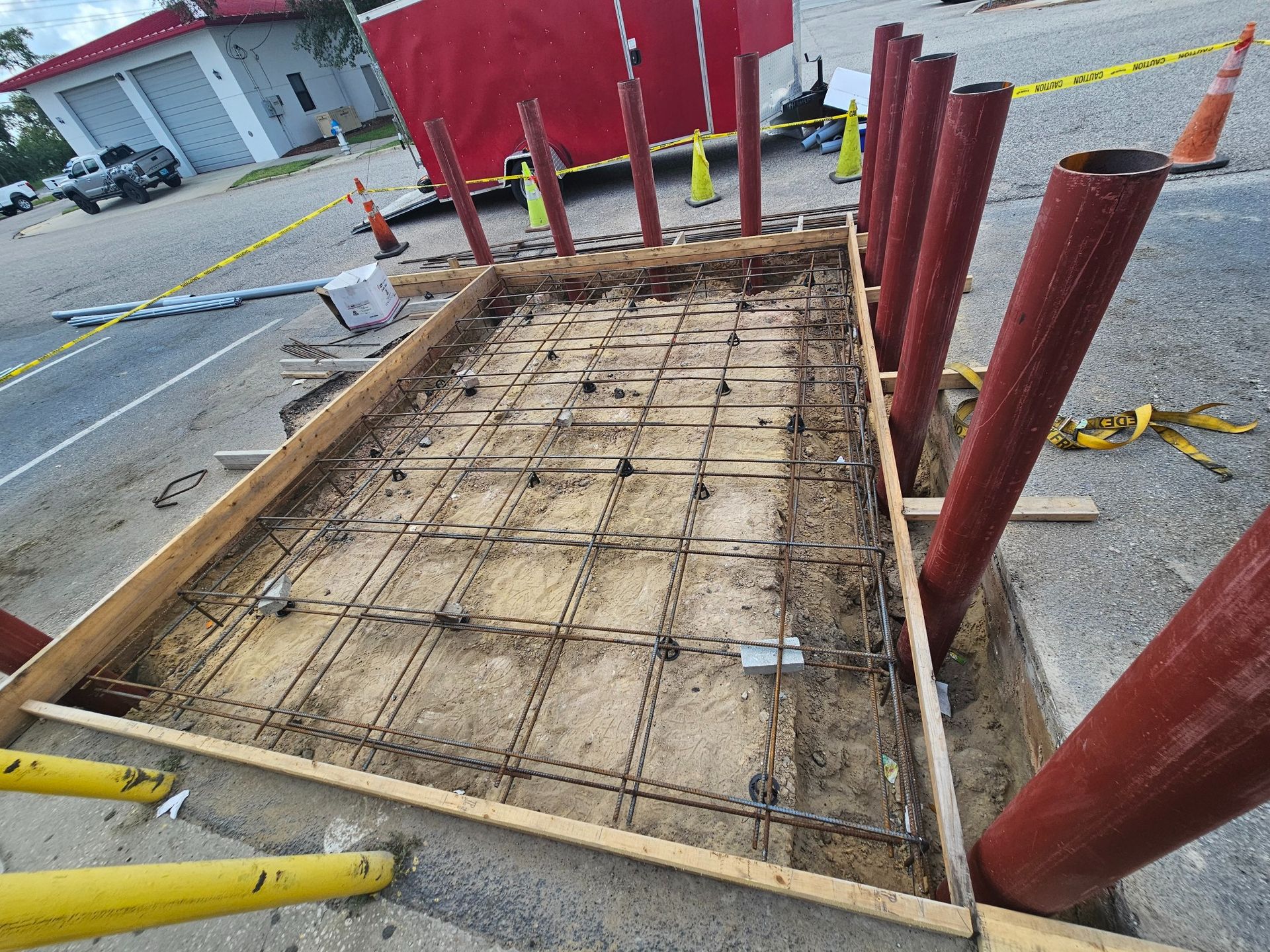 Construction site with a wooden frame, rebar grid, and red support poles on a road.