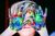 Person with hands covered in colorful paint, looking through them.