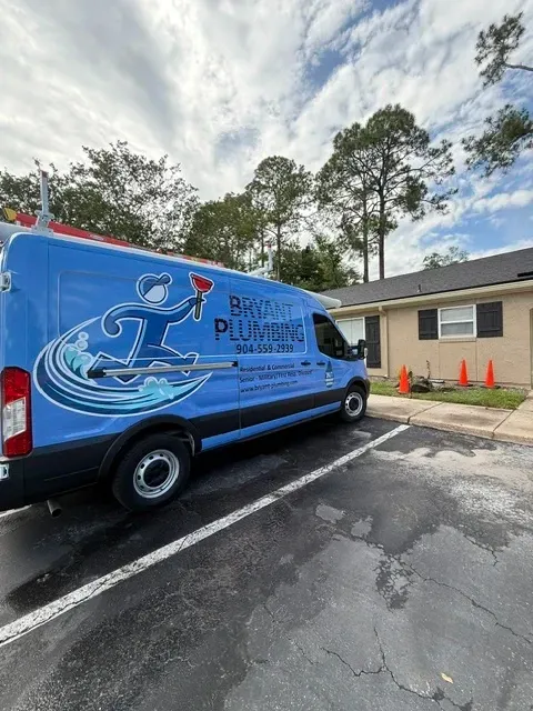 Blue delivery van with logo parked beside a building on a wet lot, with orange cones nearby