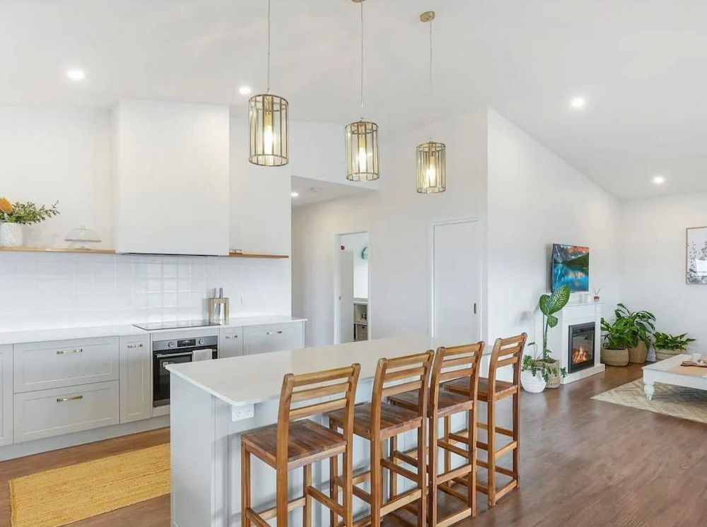 A Modern Kitchen With a White Countertop Island and Wooden Bar Stools — JGD Constructions in Yungaburra, QLD