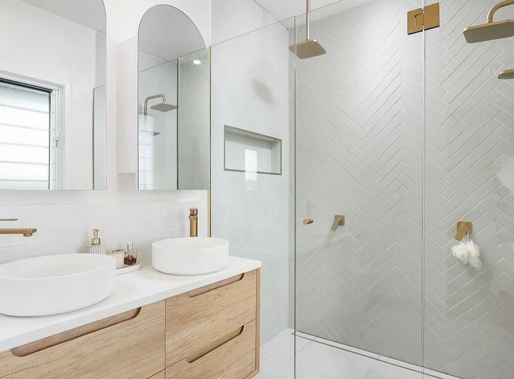 Modern Bathroom With White Herringbone Tile, Wooden Vanity, and Gold Fixtures — JGD Constructions in Lake Eacham, QLD