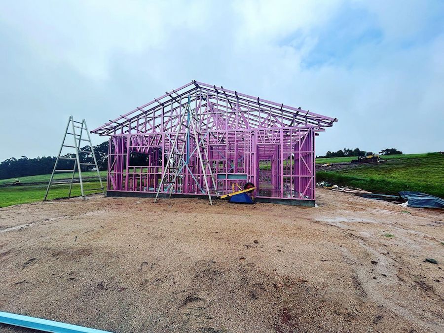 Pink Metal House Frame Under Construction on a Dirt Lot — JGD Constructions in Lake Eacham, QLD