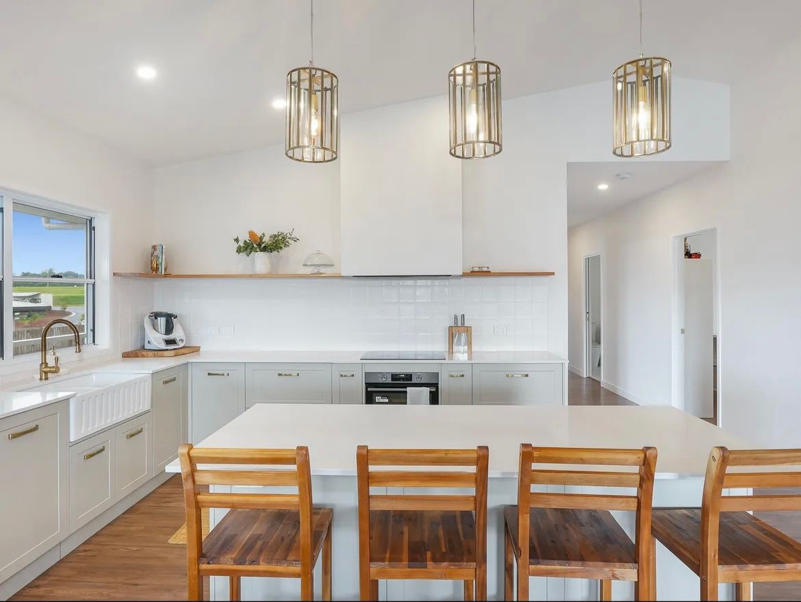Modern Kitchen With Light Grey Cabinets, White Island, Wooden Stools, And Gold Pendant Lights — JGD Constructions in Atherton, QLD